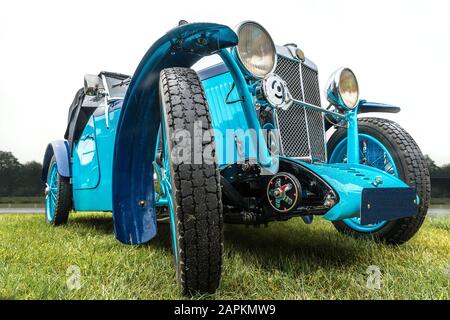 Nahaufnahme eines blauen Autos mit großen Rädern geparkt Auf einem grünen Feld Stockfoto