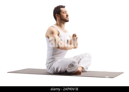 Junger Mann, der auf einer Trainingsmatte in einer Meditationsstellung sitzt, isoliert auf weißem Hintergrund Stockfoto