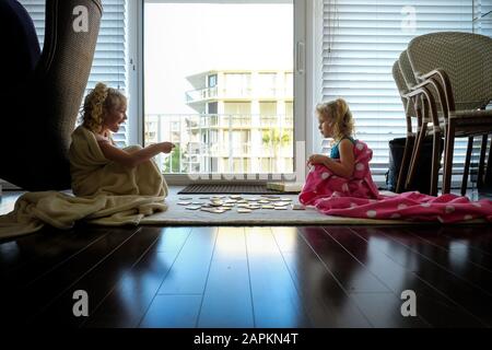 Kleine Mädchen sitzen auf dem Boden in Decken spielen Karten in Hintergrundbeleuchtung Stockfoto