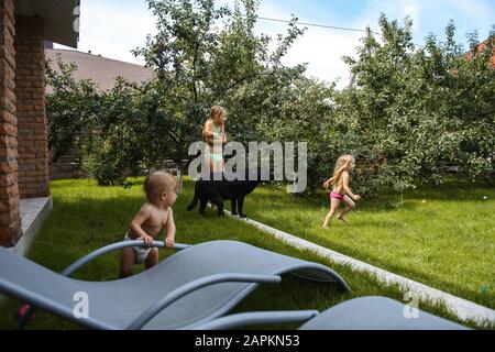 Kleines Mädchen, das mit Wasser im Hof eines Hauses mit einem schwarzen Hund spielt Stockfoto