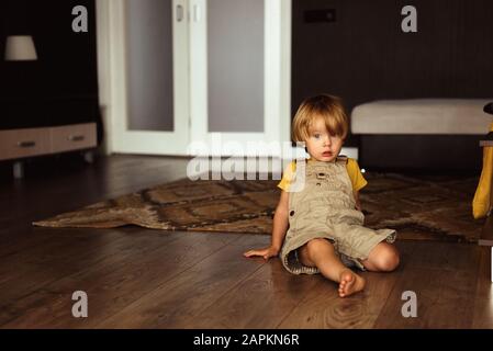 Kleiner Junge, der auf dem Teppich im Haus sitzt Stockfoto