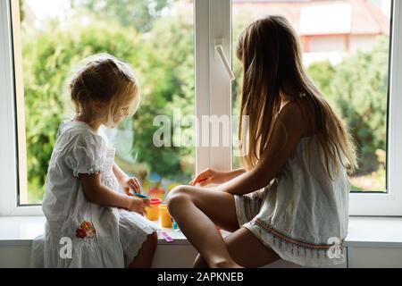 Zwei Schwestern spielen Plastilin am Fenster Stockfoto