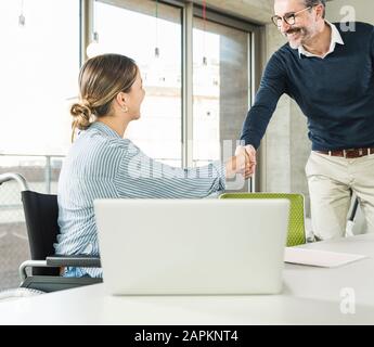 Reifer Geschäftsmann und junge Geschäftsfrau schüttelt die Hände am Schreibtisch im Büro Stockfoto