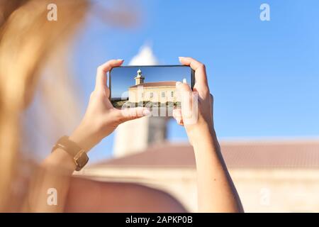 Junge Frau fotografiert den Leuchtturm von Punta Nati auf Menorca, Spanien Stockfoto