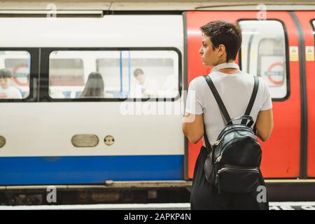 Rückansicht der Frau mit Rucksack auf dem Bahnsteig der U-Bahn, London, Großbritannien Stockfoto