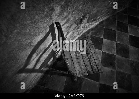 Graustufenaufnahme eines Holzstuhls in der Oberfläche von Im Hintergrund eine diamantgeflieste Form Stockfoto