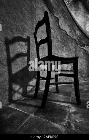Graustufenaufnahme eines Holzstuhls mit einem Schatten An der Wand Stockfoto