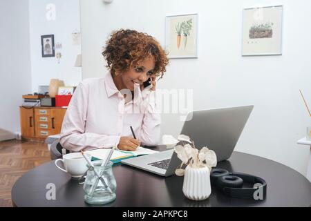 Junge Frau, die zu Hause arbeitet und telefoniert Stockfoto