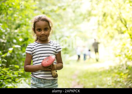 Kleines Mädchen, das im Wald steht und die Fliege agarisch hält Stockfoto