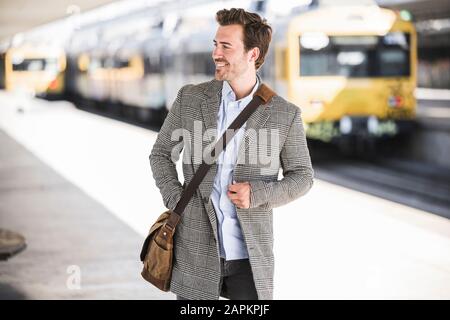 Lächelnder junger Geschäftsmann am Bahnhof, der sich umsieht Stockfoto