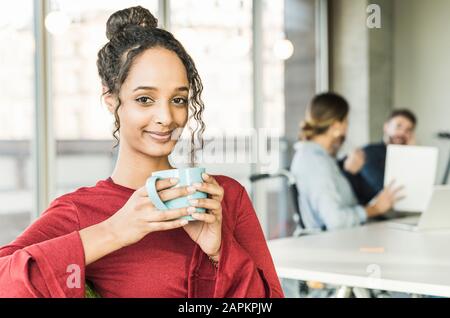 Portrait einer lächelnden jungen Geschäftsfrau, die während einer Besprechung im Büro eine Kaffeepause hat Stockfoto