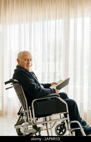 Porträt eines lächelnden älteren Mannes, der mit einem Buch im Rollstuhl sitzt Stockfoto