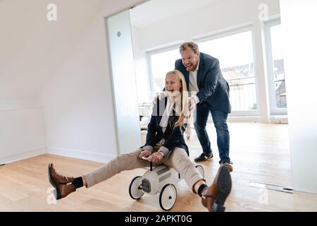 Verspielter Geschäftsmann treibt Geschäftsfrau im Büro auf Spielzeugauto Stockfoto