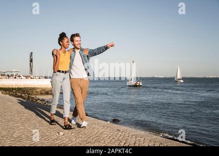 Glückliches junges Paar, das an der Anlegestelle am Wasser, Lissabon, Portugal, spazieren geht Stockfoto