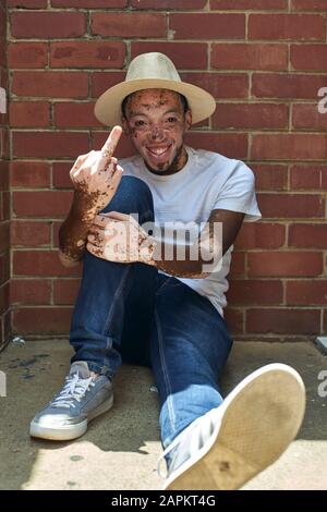 Porträt des jungen Mannes mit Vitiligo, der einen Hut trägt und den Finger gibt Stockfoto