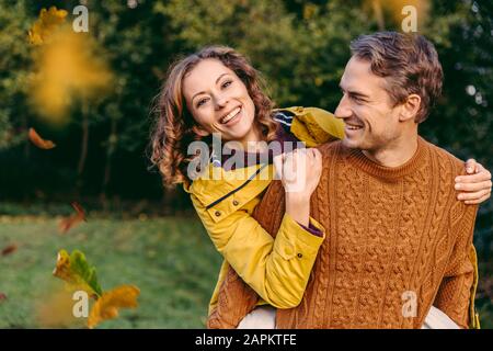 Mann, der Frau im Herbst eine Huckepackfahrt im Freien beschaute Stockfoto