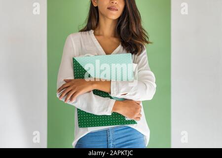 Schnittansicht der jungen Geschäftsfrau, die vor der grünen Wandhaltermappe steht Stockfoto