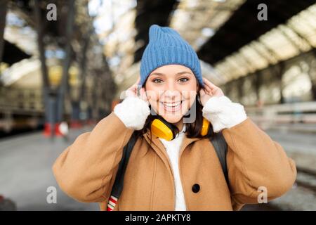 Porträt einer glücklichen jungen Frau, die am Bahnhof einen wolligen Hut trägt Stockfoto