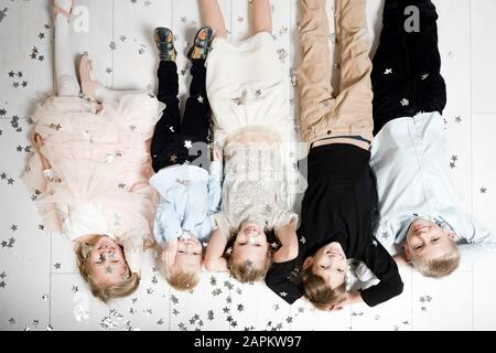Gruppenbild von fünf Kindern, die auf dem Boden auf dem Kopf liegen und von Weihnachtskonfetti bedeckt sind Stockfoto
