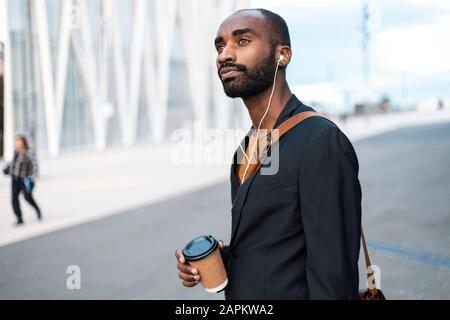 Porträt eines jungen Geschäftsmannes mit Kaffee zum Musikhören mit Kopfhörern im Freien Stockfoto