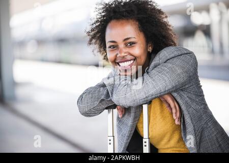 Porträt einer lächelnden jungen Geschäftsfrau mit Koffer am Bahnhof Stockfoto