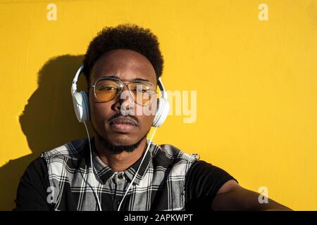 Porträt des jungen Mannes, der Musik mit Kopfhörern an der gelben Wand hört Stockfoto