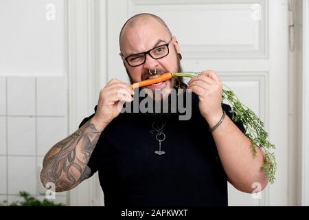 Porträt des bärtigen Mannes, der in Karotte in der Küche beißt Stockfoto