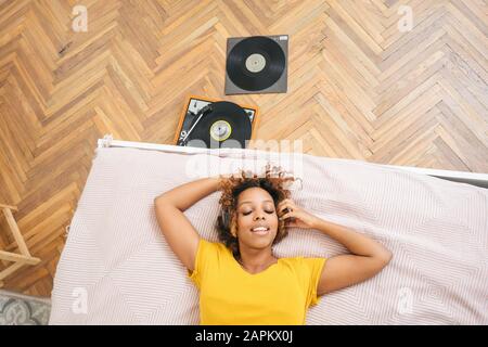 Junge Frau, die auf dem Bett liegt und Musik mit Kopfhörern und Plattenspieler hört Stockfoto