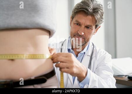 Doktor, der Taille der weiblichen Patientin in seiner medizinischen Praxis misst Stockfoto