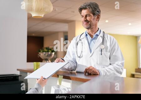 Arzt, der in seiner Arztpraxis an der Rezeption eine Krankenakte einzieht Stockfoto