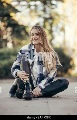 Porträt einer lächelnden jungen Frau, die draußen auf dem Boden sitzt Stockfoto