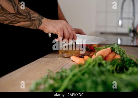 Nahaufnahme des tätowierten Mannes, der Karotten in der Küche verwahrt Stockfoto