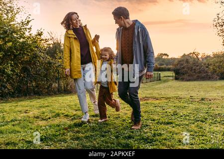 Eltern mit Tochter gehen im Herbst auf eine Wiese Stockfoto