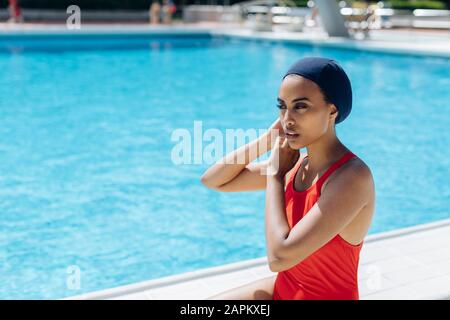 Portrait der jungen Frau, die am Pool eine Schwimmkappe aufsetzt Stockfoto