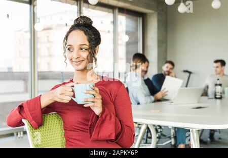 Lächelnde junge Geschäftsfrau, die während einer Besprechung im Büro eine Kaffeepause hat Stockfoto