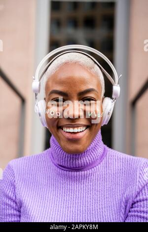 Portrait einer weißen, haarigen Frau mit weißen Kopfhörern und Aufklebern im Gesicht, gute Stimmung Stockfoto