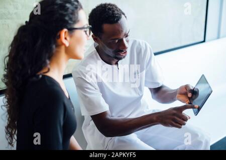 Zahnärztin mit Tablette spricht mit weiblicher Patientin in der Zahnchirurgie Stockfoto