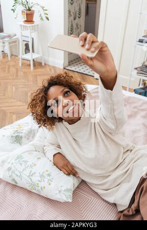 Glückliche junge Frau, die im Bett liegt und eine selfie nimmt Stockfoto