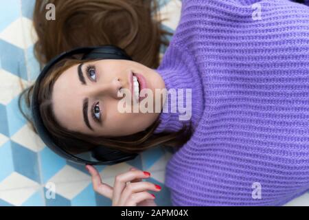 Porträt der jungen Frau, die auf dem Boden liegt Musik mit Kopfhörern hören Stockfoto
