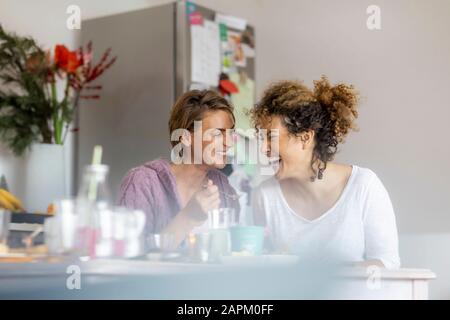 Zwei glückliche Frauen sitzen und reden zu Hause am Küchentisch Stockfoto
