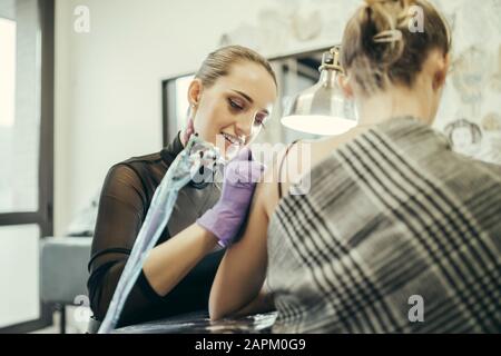 Tätooistische Frauen, die den Oberarm der weiblichen Kundin tätowieren Stockfoto