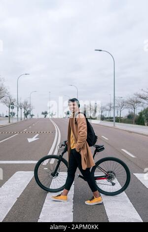 Junger Mann mit Fahrrad, der eine Straße in der Stadt überquert Stockfoto