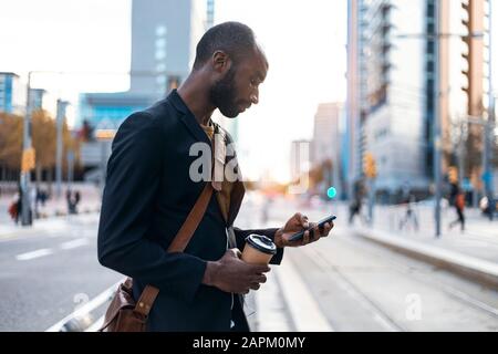 Junger Geschäftsmann mit Kaffee für den Blick auf das Smartphone Stockfoto