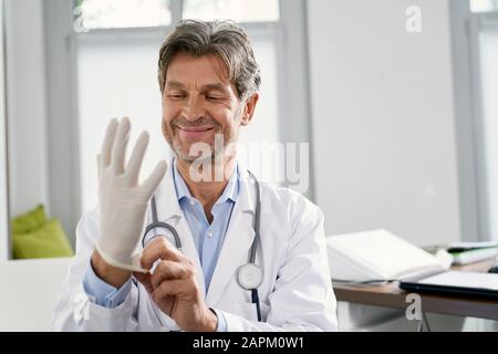 Arzt, der in seiner Arztpraxis Schutzhandschuhe anlegt Stockfoto
