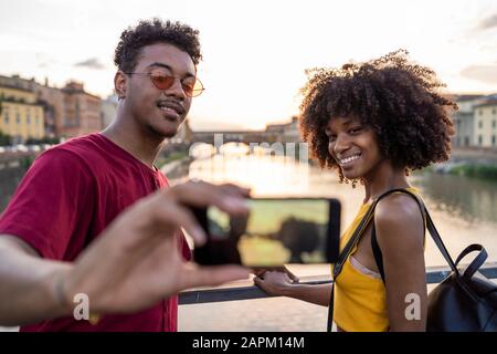 Junges Touristenpaar mit selfie auf einer Brücke über dem Arno bei Sonnenuntergang, Florenz, Italien Stockfoto