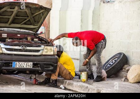 Zwei kubanische Männer fixieren einen flachen Reifen auf ihrem Auto; Santiago de Cuba, Kuba. Stockfoto