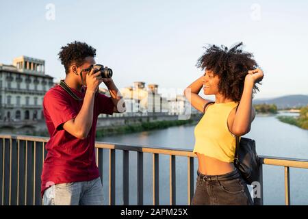 Junger Mann, der bei Sonnenuntergang auf einer Brücke über dem Arno ein Bild von seiner Freundin macht, Florenz, Italien Stockfoto