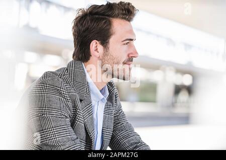 Porträt des jungen Geschäftsmannes, der am Bahnhof sitzt Stockfoto