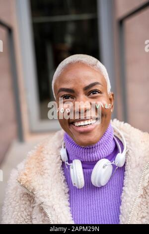 Portrait einer reifen weißen, haarigen Frau mit weißen Kopfhörern und Aufklebern im Gesicht, gute Stimmung Stockfoto