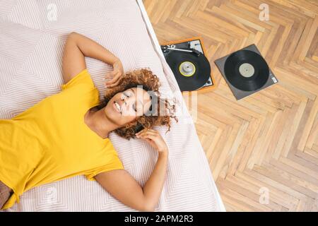 Junge Frau, die auf dem Bett liegt und Musik mit Kopfhörern und Plattenspieler hört Stockfoto